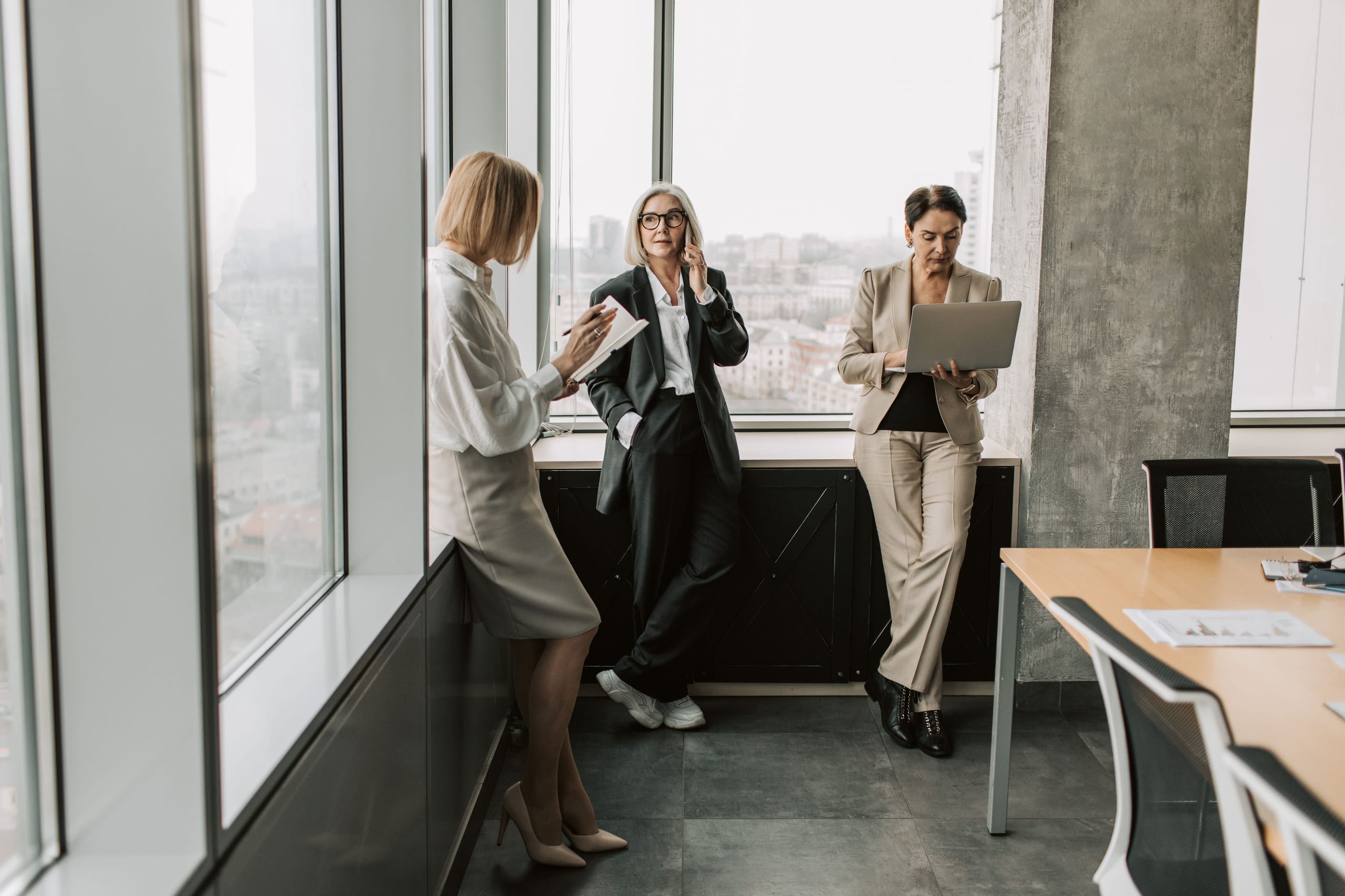 Three agents working side by side at the office window, one on a call, one on a tablet, one on a laptop